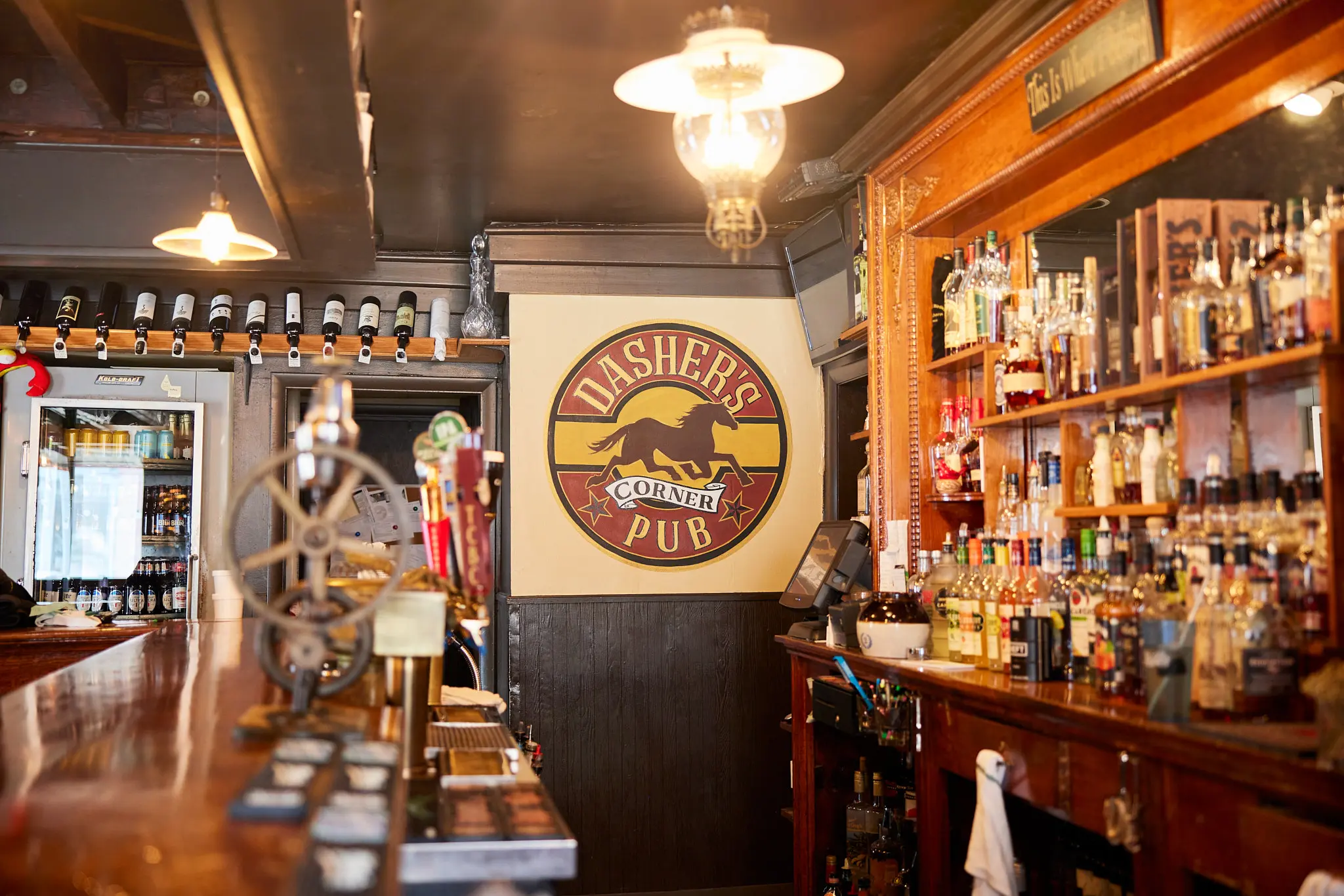 warm pub interior with a logo, shelves of wine and spirits, and a bar counter